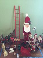 Group of wooden Christmas decor items including large Santa figure, red ladder, reindeer planter, sleigh, stars, and multiple figurines arranged on a table.