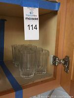 Eight ribbed drinking glasses inside a cabinet on corrugated cardboard.