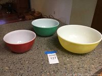 Three nesting Pyrex bowls in red, green, and yellow on a kitchen counter, showing the complete visible lot items.