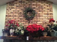 Wide view of floral arrangements on mantle with hanging wreath above on brick wall