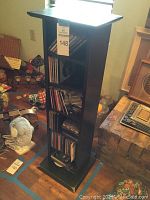 Front angled view of the black wooden CD stand filled with CDs on multiple shelves showing condition and content.