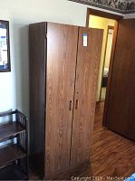 Front view of tall storage cabinet with two doors, woodgrain laminate surface, metal handles, and keyhole.