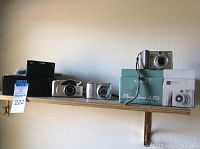 Wide shot of all cameras on wooden shelf showcasing Canon PowerShot in box, Kodak camera, silver and black cameras.
