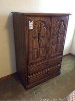Closed wooden wardrobe showing decorative carved doors with handles and lower drawers.