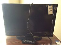 Front view of Dynex 26-inch TV showing screen and remote on table.