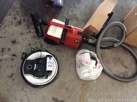 Two vacuum cleaners including a Shark robotic vacuum cleaner and a red Eureka upright vacuum with hose.