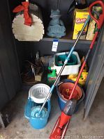 Photo showing mop bucket with wringer, red and blue handled mops, storage bins, cleaning liquids, and decorative blue frog welcome sign