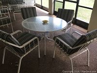 View of round patio table with four cushioned chairs arranged around it on enclosed porch.