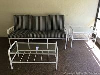 Full view of patio couch with striped cushions and matching coffee and end tables with white metal frames.