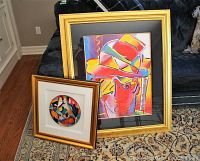 Two gold-framed artworks leaning on floor; small circular abstract and large rectangular portrait
