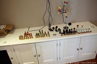 Chess pieces and a medieval knight figurine displayed on a white sideboard against a grey wall, showing various colored sets including red, green, black, and white.
