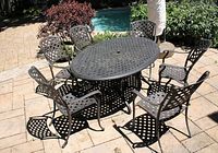 Six metal lattice chairs arranged around oval metal table on stone patio