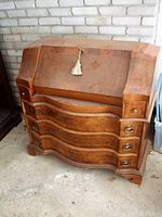 Front view of secretary desk showing serpentine front drawers and closed drop-front with tassel key