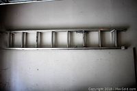 Full side view of the aluminum extension ladder hung horizontally against a wall showing the full length and rung arrangement.