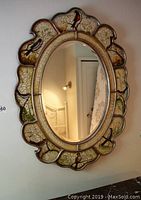 Full view of the oval wooden framed mirror with bird motif and scalloped edges hanging on a wall.