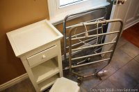 View of two chrome-finish heated towel racks along with the white wooden cabinet and white plastic step stool on tiled floor