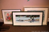 Framed art pieces arranged on floor: one large rectangular print of Georgian Bay landscape, two smaller framed watercolours of flowers and ice flows, showing condition and framing.