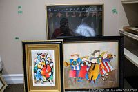 Three framed artworks leaning against a wall: NYC Opera Falstaff poster in black frame, colorful cubism style music print in gold frame, whimsical children musicians print in black frame with gold inner border.