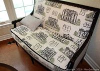 Bench placed near window showing full front and side profile, upholstery with architectural prints and pillow visible.