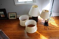 Shows three lamps and two lamp shades arranged on wooden floor near window to display condition and style.