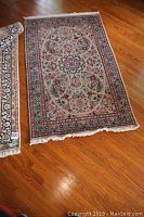 Photo of rectangular woven area rug on hardwood floor showing full pattern, floral central medallion and border.