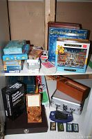Overall view of the game and puzzle lot on shelves showing board games, card decks, Nintendo Game Boy console and cartridges.