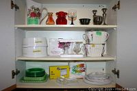 Photo inside cabinet showing various glassware including mugs, dessert plates, bowls, disposable items, and silver candlesticks