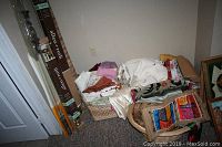 Photo of Allen Roth drapery rods boxed and standing upright near a corner wall next to baskets with assorted folded fabrics and linens.