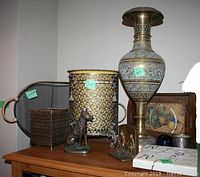 Wide shot showing all brass finish decor items on top of wooden dresser including tray, vases, dog doorstop, bookends, ceramic plaque, glass paperweight and framed picture.
