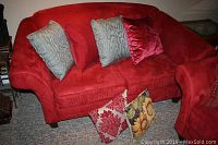 Full front view of red microfiber loveseat with four pillows on seat and two on floor