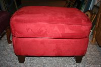 Front view of red microfiber ottoman showing padded cushion and wooden legs with minor scuffs.