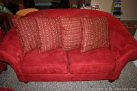 Front angle view of red microfiber loveseat with four patterned throw pillows on carpeted floor.