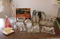 Photo showing entire assortment of glassware and serving ware on table including rose glass decanter, cut glass stemware, and accessories.