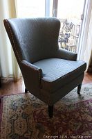 Side angle view of blue-gray upholstered armchair showing wingback design, nailhead grommet trim, and tapered legs.