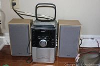 Front view of Sony CMT-EH10 micro HiFi stereo system with two speakers, remote on top, and antenna behind.