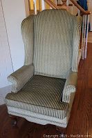 Front view of the upholstered wingback armchair showing the striped fabric upholstery and wooden legs.