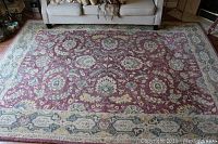 Full view of the large rectangular Persian-design wool rug with a red field and cream/green border, placed on hardwood floor in living room setting.