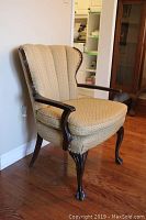 Side angle view of upholstered chair showing curved wood arms, padded backrest with vertical channels, and cabriole clawfoot legs.