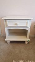 Front view of white wooden bedside table showing drawer and open shelf.