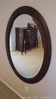 Large oval mirror mounted on a beige wall, showing reflection of room furniture.