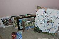 Group photo showing the collection of prints and paintings stacked against wall, including the large floral painting and various framed landscapes and prints.