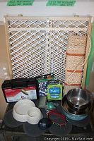 Photo showing the entire lot including the metal pet gate, bowls, toys, scratching board, grooming tools, collars, mat, and bandana arranged on table.