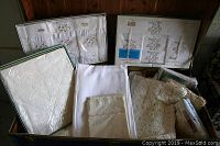 Opened green suitcase containing packaged linens, unboxed linens and crocheted blankets.