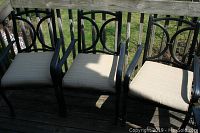 Three black metal frame patio chairs with beige cushions aligned side by side outdoors on a wooden deck.