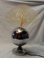 Full view of vintage fibre optic lamp with chrome base and lit optic strands glowing orange and yellow.