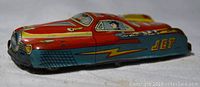 Front and side views of the red, blue, and yellow vintage tin litho toy car showing the 'JET' graphics and a cartoon driver inside the windows. Metal wheels are visible underneath.