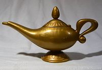 Full side view of the plastic gold-colored Aladdin's lamp showing its shape and hinged lid on top.