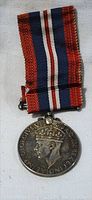 Full view of the medal with ribbon laid flat on a white surface showing whole ribbon and obverse side of medal.