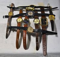 Full view of 10 assorted wristwatches laid flat showing cases and straps, various shapes and metals.
