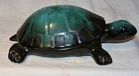 Side view of ceramic turtle figurine showcasing blue-green and black coloration with a glossy finish.